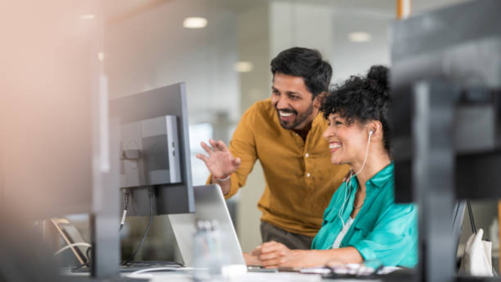 Coworkers in front of computer monitor in modern office chatting online.