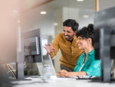 Coworkers in front of computer monitor in modern office chatting online.